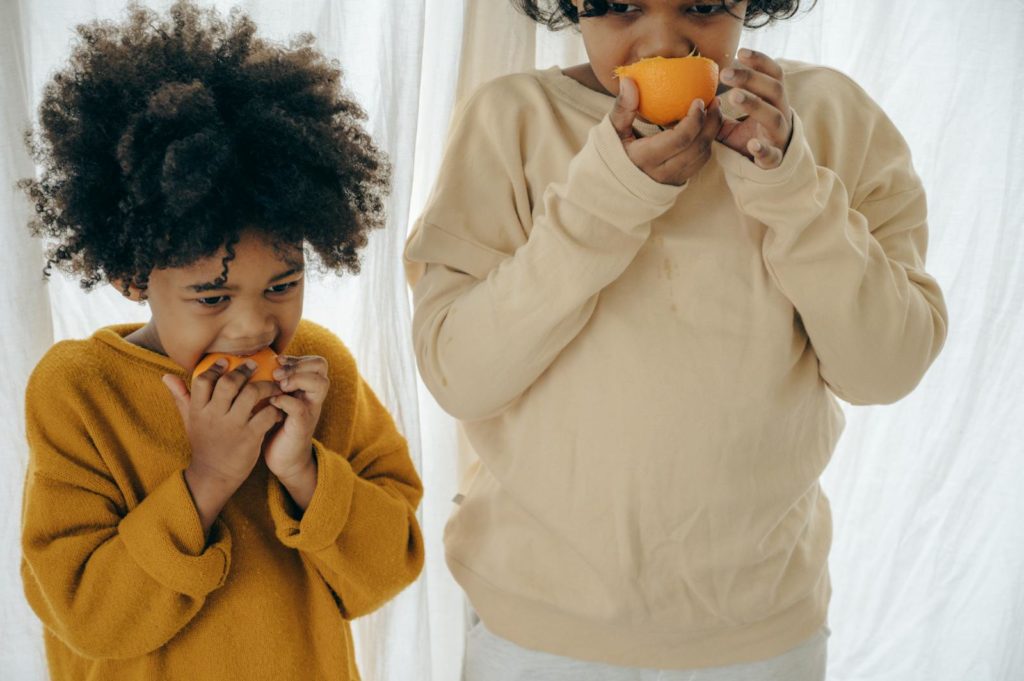 African American kids standing together and eating sweet oranges while resting in modern studio on daytime